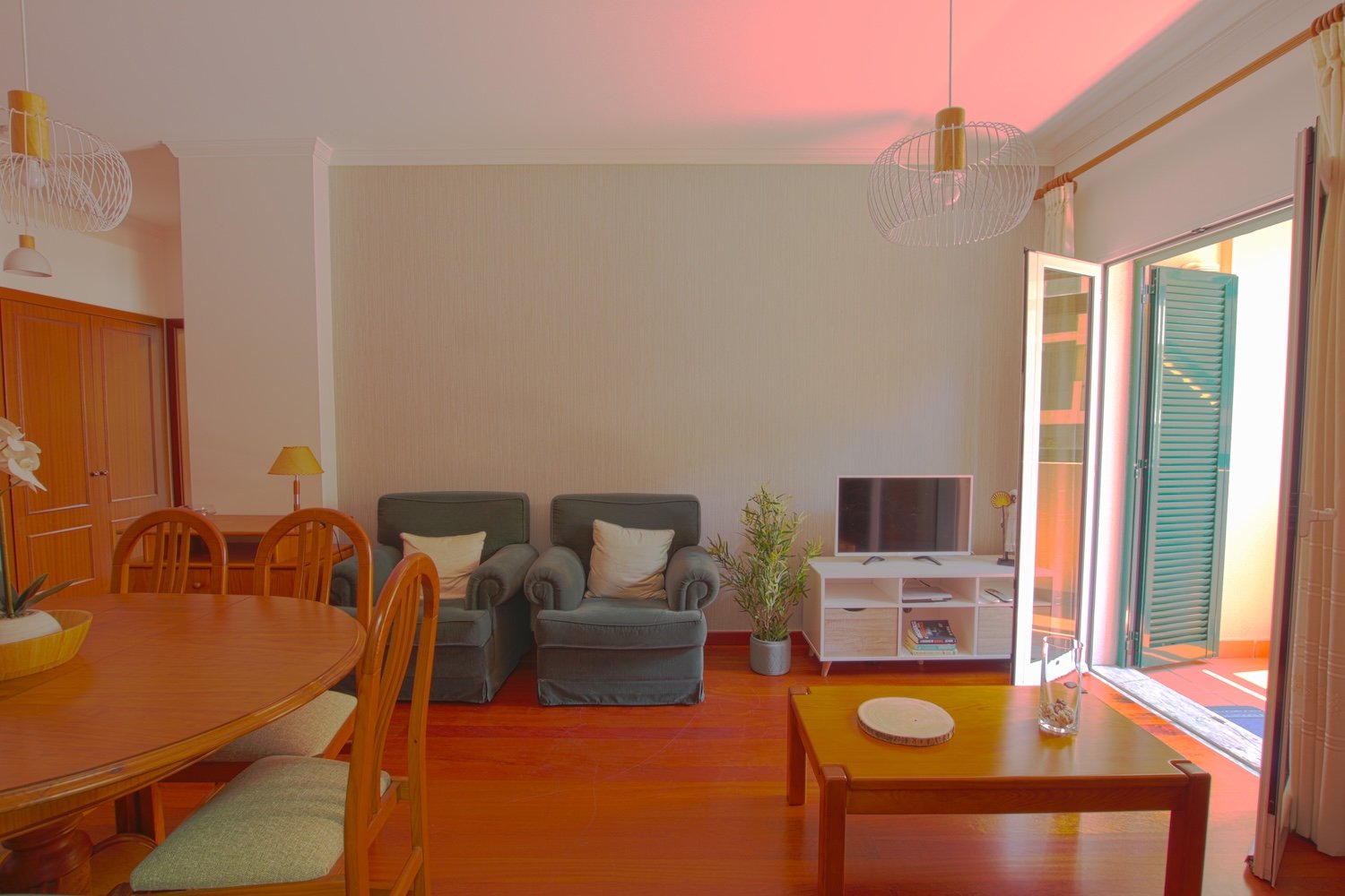 Lounge with tv area, two armchairs, a dining table its chairs and access to the veranda