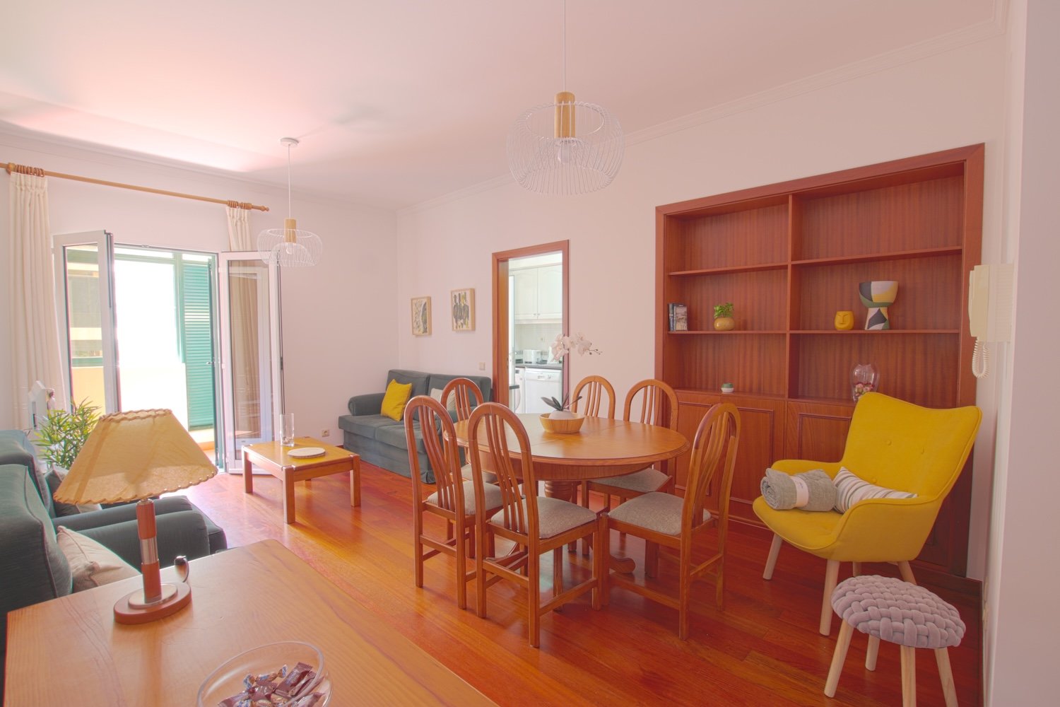 The living room showing the dining table, its chairs, two armchairs, a sofa and the access to the veranda