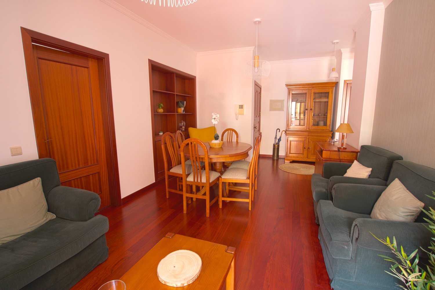 The lounge with a sofa, two armchairs, a dining table and its chairs access to the kitchen and a shelf